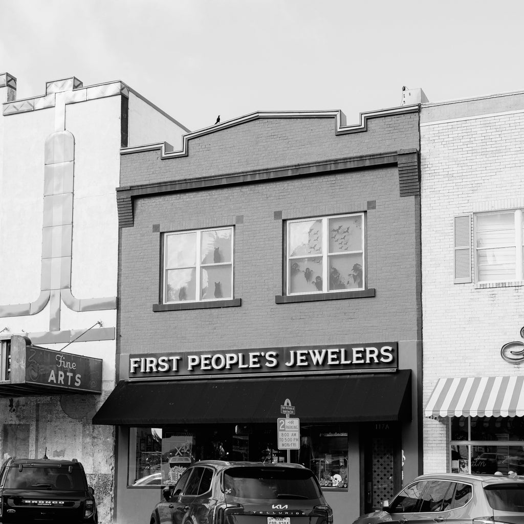 Black and white photo of a building with 'First People's Jewelers' sign on a street corner.